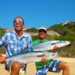 Two men showing off their large fish on the beach that they just caught