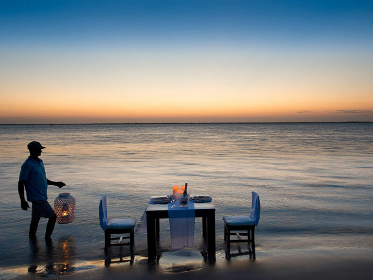 romantic dining set up of table and chairs on the beach of mozambique during sunset