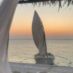 A Dhow docked off in the ocean with the sunset in the back